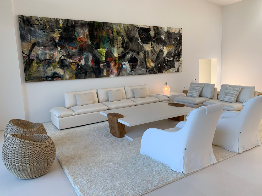 large white living room with a unique coffee table and dark panoramic painting on the wall
